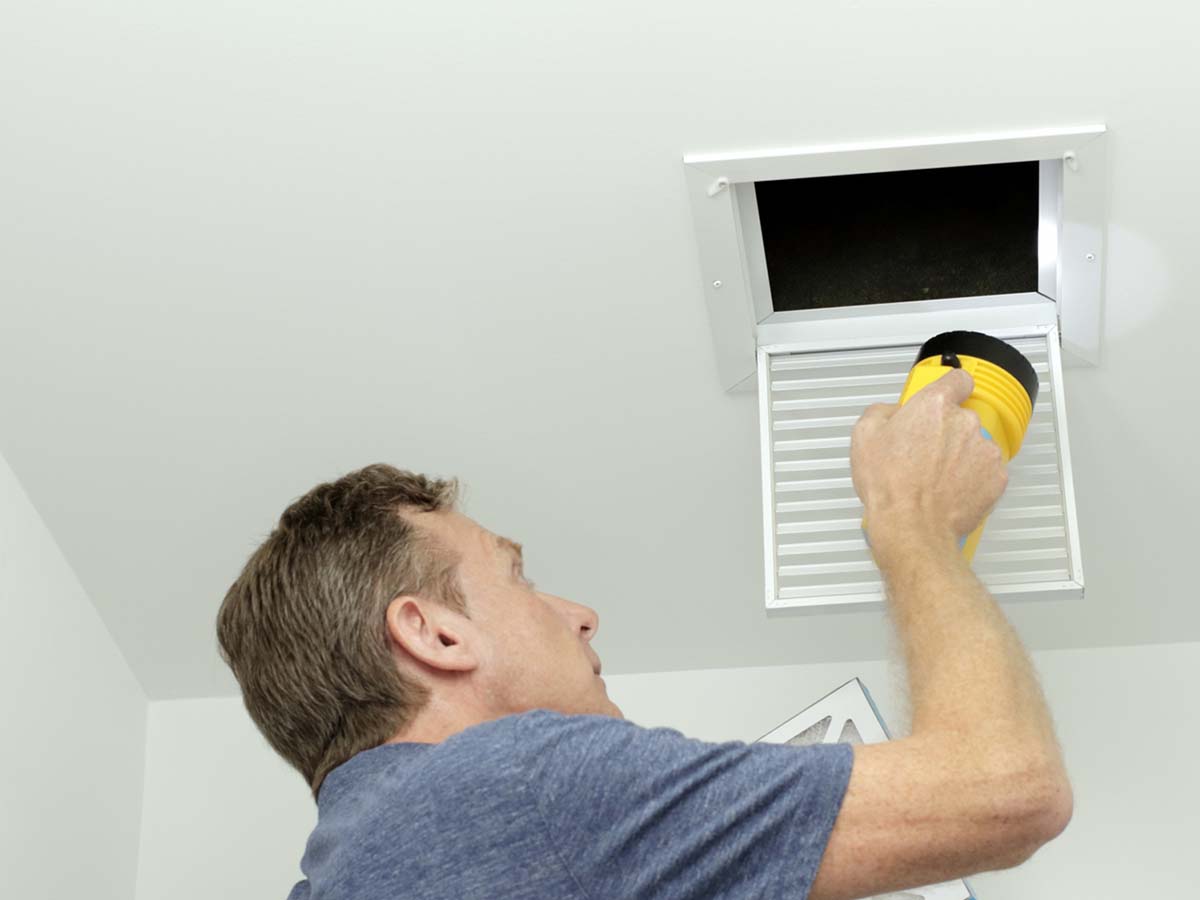 An image of a man shining a flashlight into a vent.