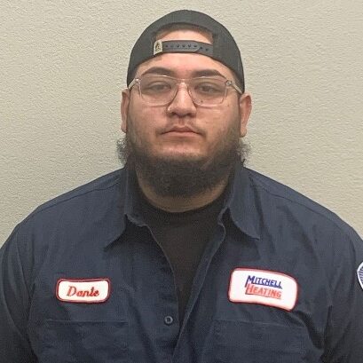 Portrait of Dante Vigil, a member of the service team at Mitchell Heating, wearing glasses, a cap, and a dark blue uniform.