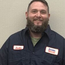 Portrait of Justin, a technician at Mitchell Heating, smiling and wearing a dark blue uniform with a name tag.